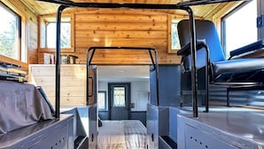 Un interior compacto estilo cabaña con techo de madera, cama con estructura metálica y pequeña zona de kitchenette.