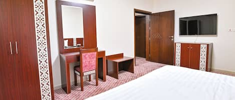 Una habitación de hotel con cama, escritorio, silla, armario y televisor.