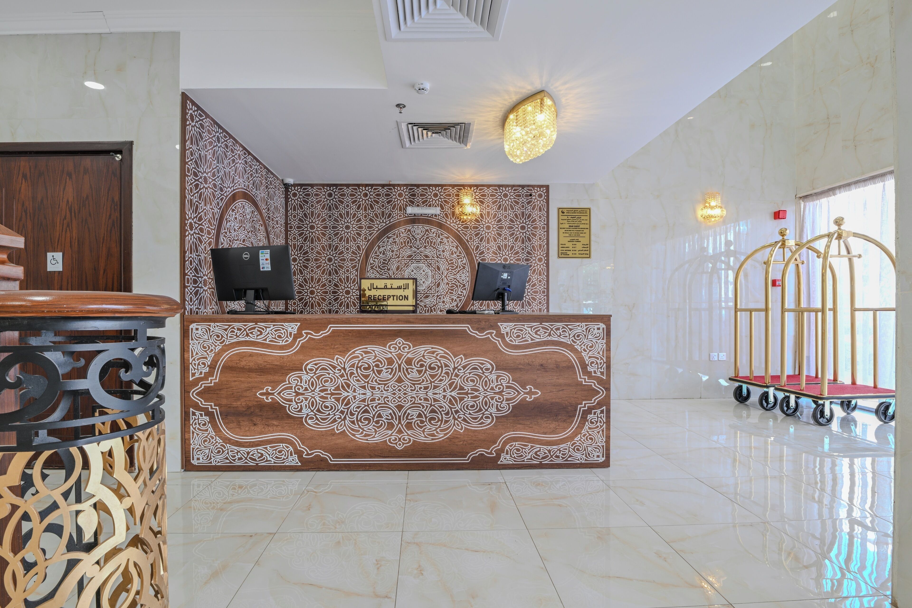 A reception area with a marble floor, a reception desk with a decorative panel, a computer, and a cart with a red mat.