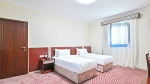 A hotel room with two beds, a wooden wardrobe, a nightstand, and a window with curtains. - Diyar AlSaliheen Serviced Apartments (Madinah)
