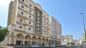 A multi-story hotel with a central courtyard, arched entrances, and a clock tower. - Diyar AlSaliheen Serviced Apartments (Madinah)