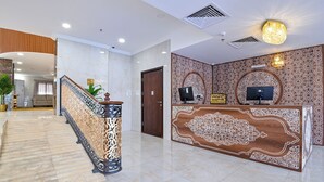 A reception area with a wooden reception desk, a staircase with decorative railings, and a patterned wall. - Diyar AlSaliheen Serviced Apartments (Madinah)