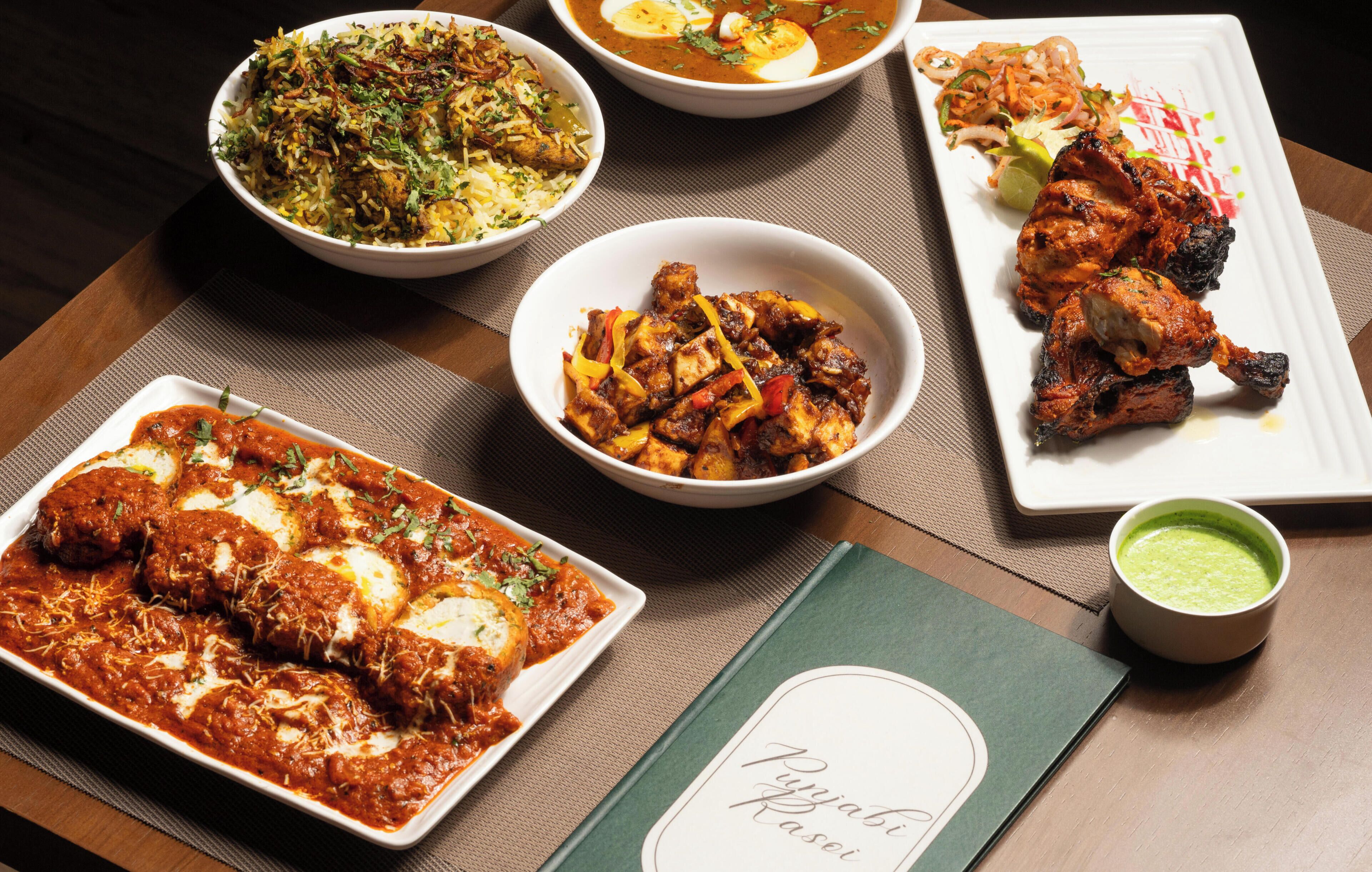 A variety of dishes on a table, including a bowl of rice, a plate of chicken, and a bowl of curry.