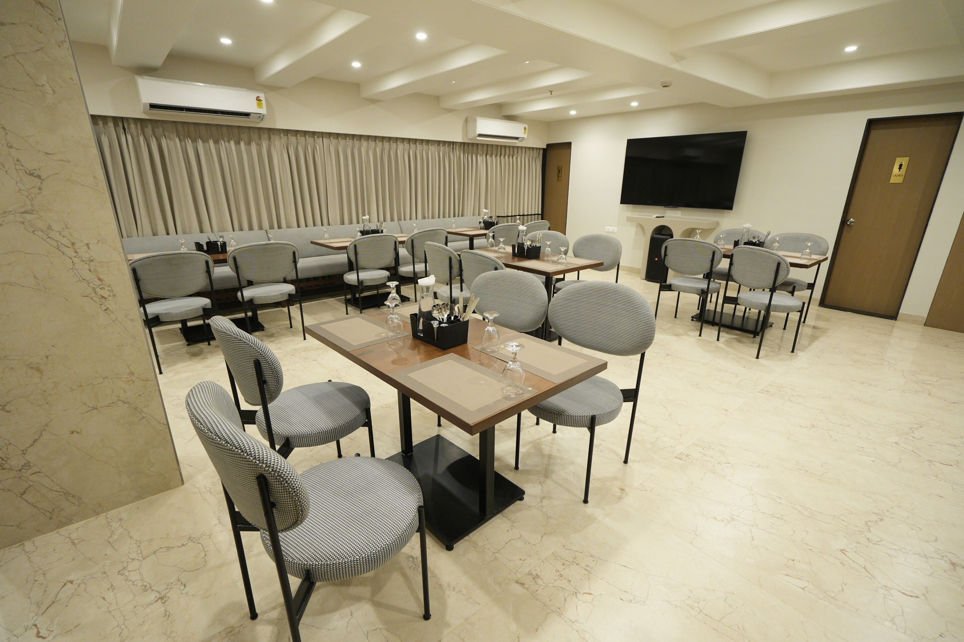 A hotel conference room with a long table, multiple chairs, a sofa, and a TV screen.