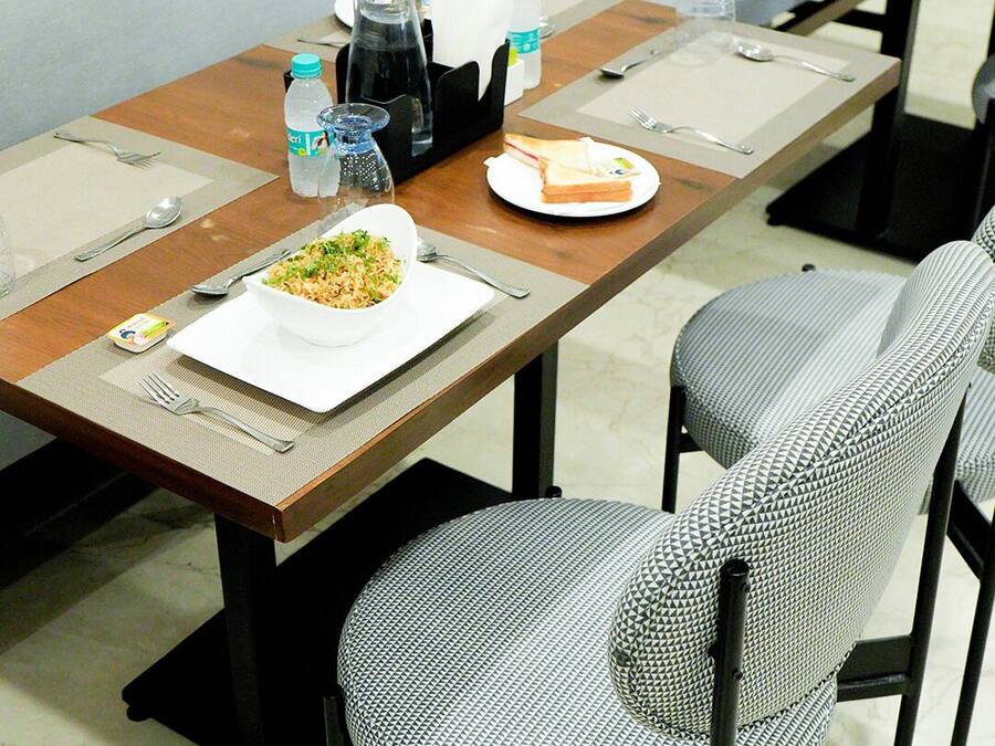 Un comedor con una mesa preparada para dos personas, con platos, cubiertos y una botella de agua.