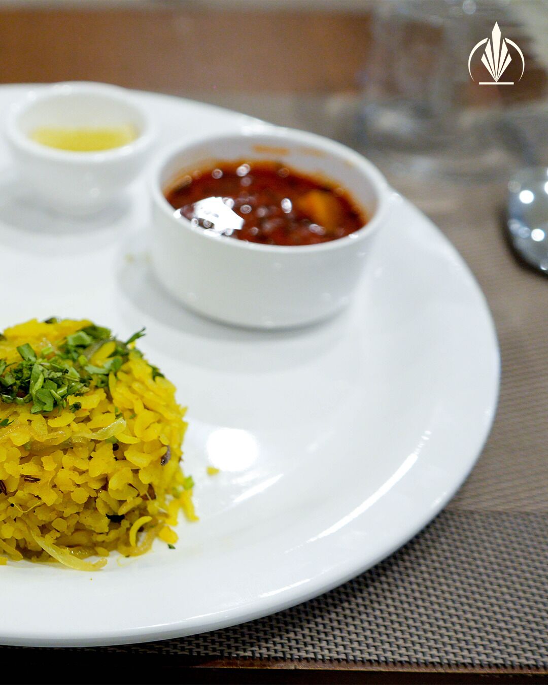 Un plato de arroz amarillo adornado con hierbas, acompañado por dos recipientes pequeños de salsa.