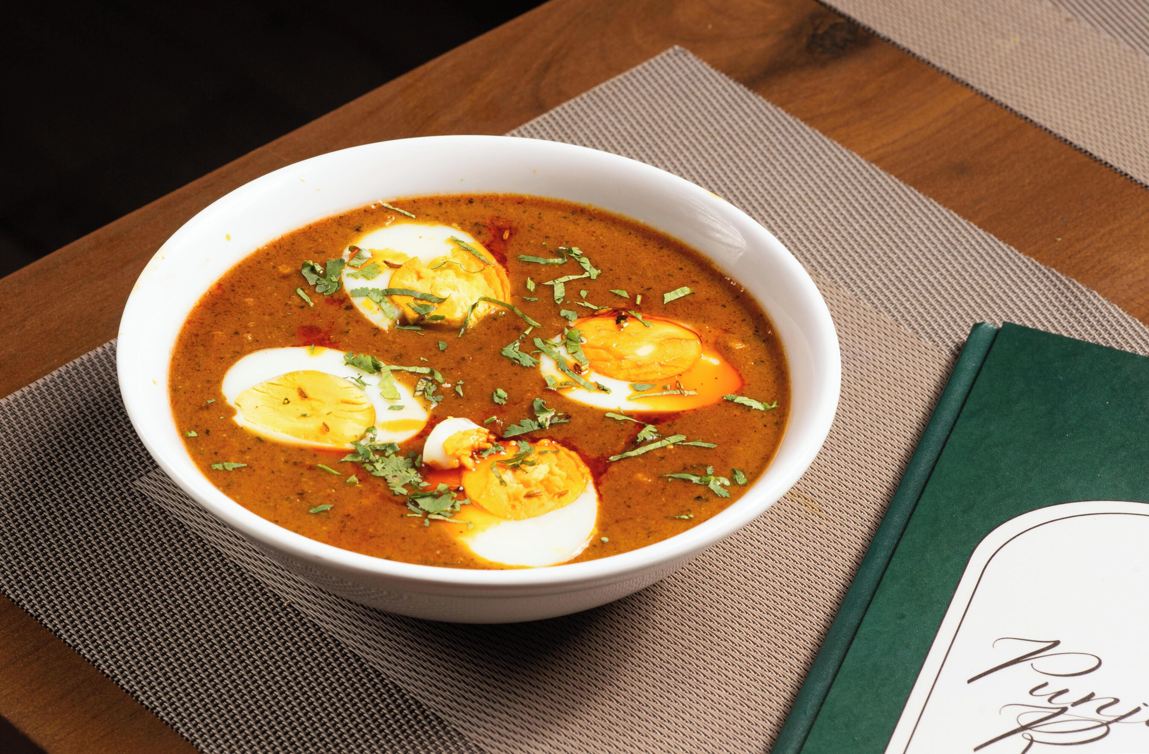 A bowl of soup with eggs and herbs on a table with a placemat and a green book.