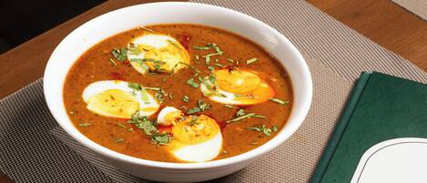 A bowl of soup with eggs and herbs on a table with a placemat and a green book.