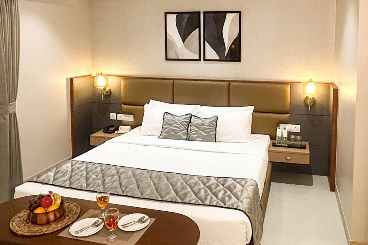 Ein Hotelzimmer mit Bett, Nachttischen, einem Schreibtisch mit Stuhl, einer Obstschale und einer Weinflasche.
