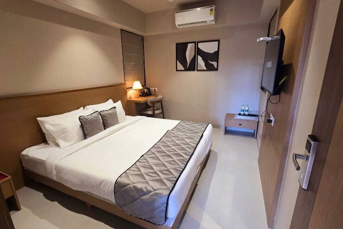 Ein Hotelzimmer mit Bett, Nachttisch, Lampe und einem an der Wand befestigten Fernseher.