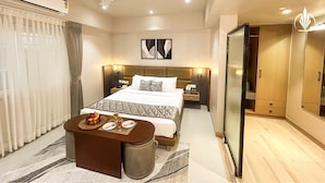 A modern hotel room with a large bed, bedside tables, a small seating area with a table and a fruit bowl, and a wardrobe. - SIVANTA BY BOMBAY GROUP OF HOTELS NAGPUR (Nagpur)