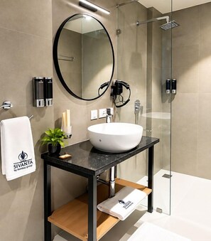 Une salle de bain moderne avec un miroir rond, un lavabo blanc et une cabine de douche en verre.