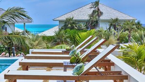 A poolside area with lounge chairs and a view of the ocean. - Brand New Villa on Pink-Sand Beachfront Estate with Shared Pool (Governors Harbour)