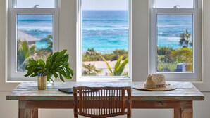 A wooden table with a chair in front of a window overlooking a beach. - Brand New Villa on Pink-Sand Beachfront Estate with Shared Pool (Governors Harbour)