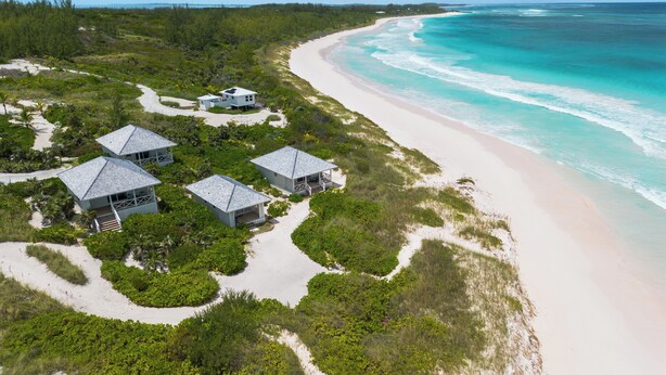 An aerial view of a coastal property with multiple buildings, a sandy beach, and a clear view of the ocean. - Brand New Villa on Pink-Sand Beachfront Estate with Shared Pool (Governors Harbour)