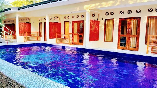 Una piscina con borde de azulejos, cubierta de madera y cortinas rojas en las ventanas.