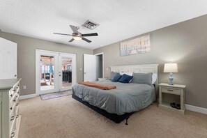 A bedroom with a bed, a nightstand, a ceiling fan, and a door leading to another room.