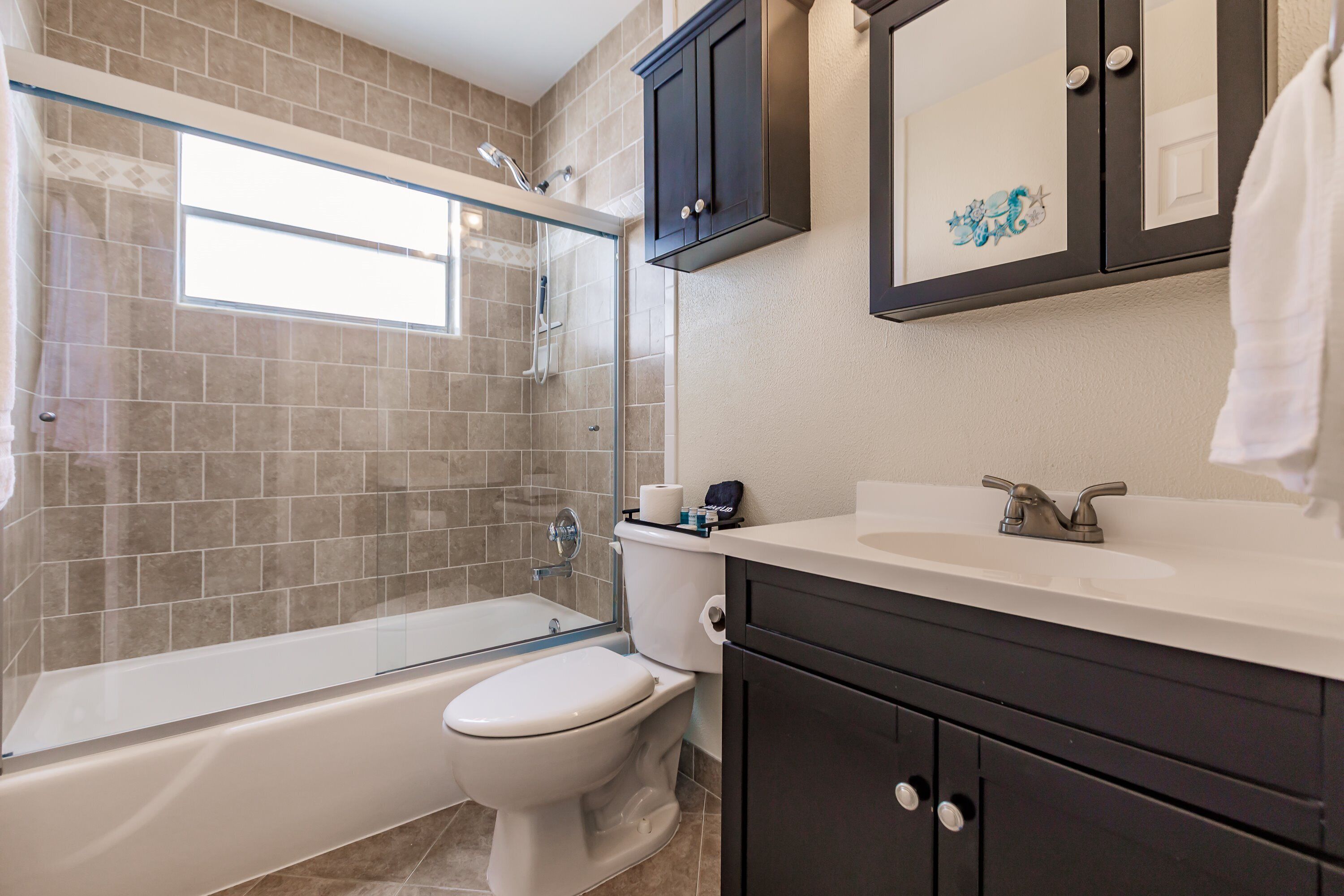 Une salle de bain avec une douche à parois de verre, des toilettes blanches et des meubles sombres.