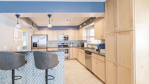 A modern kitchen with a central island, bar stools, and a tiled backsplash. - 2 Homes, 1 Private Pool Near IMG & AMI (Bradenton)