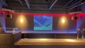 A reception area with a wooden counter, two wall-mounted speakers, and a large screen displaying a landscape scene. - YOUTEI2 (Rusutsu)