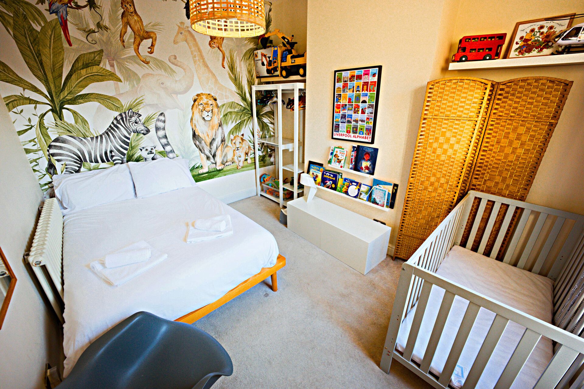 A child's bedroom with a bed, a crib, a bookshelf, and a wall mural.