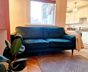 A living room with a dark blue sofa, a patterned rug, a potted plant, and a window with a view of a building.
