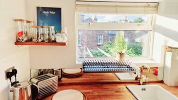 A kitchen with a wooden countertop, a sink, a kettle, a toaster, and a window with a view of a brick building and greenery.