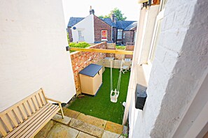 Un petit espace extérieur, avec un banc en bois, une balançoire et un petit abri de jardin.