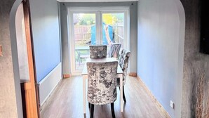 A dining area with a table and chairs, a view of the backyard through a glass door, and a concrete wall. - Ashford Blissful Retreat Modern 3-bed House (Ashford)