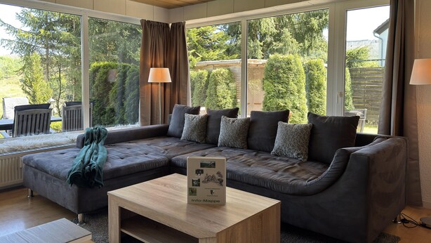 Un salon moderne avec un canapé d’angle, une table basse et de grandes fenêtres donnant sur le jardin.
