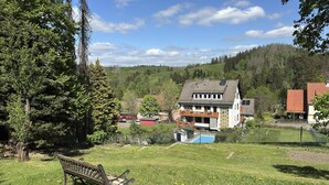 Une maison avec un grand jardin devant, un banc et une piscine.