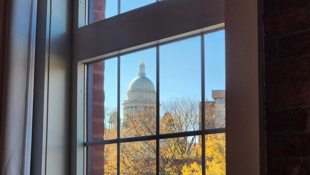 A window with a view of a building with a dome, likely a capitol, through a grid pattern. - Jennifer’s Penthouse Loft | State House City Views (Providence)
