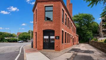 A red brick building with a black door and windows, located at a street corner with a sidewalk and trees.