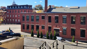 A red brick building with multiple windows and a chimney, adjacent to a larger building with a dome. - Jennifer’s Penthouse Loft | State House City Views (Providence)