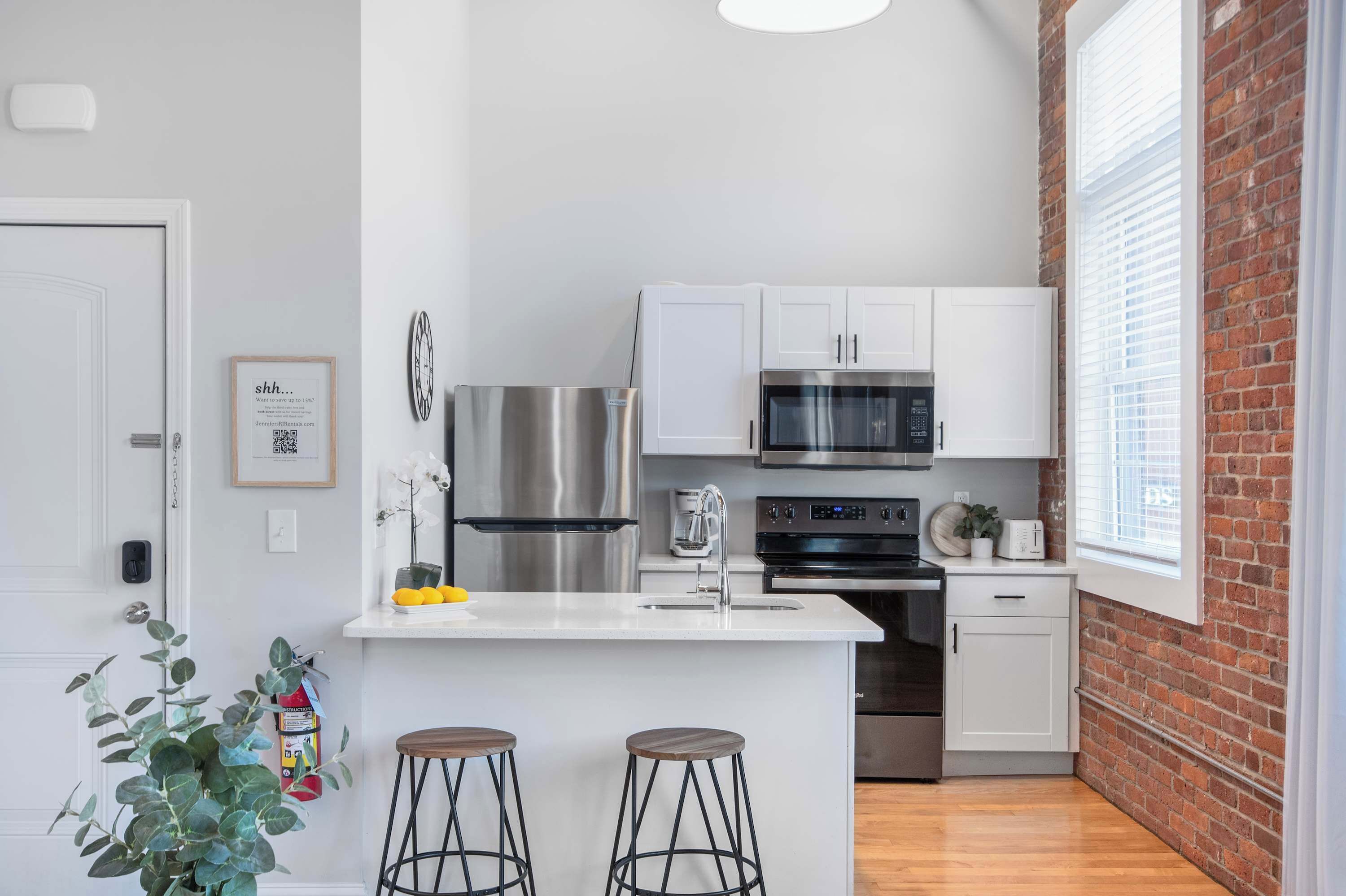 A modern kitchen with white cabinets, stainless steel appliances, and a brick wall.
