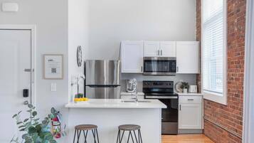 A modern kitchen with white cabinets, stainless steel appliances, and a brick wall.
