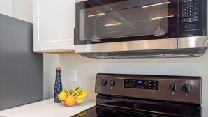 A kitchen with a stainless steel microwave, a black stove, and a fruit bowl on the counter. - Jennifer’s Penthouse Loft | State House City Views (Providence)