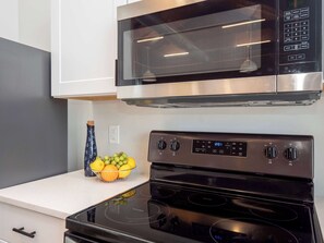 A kitchen with a stainless steel microwave, a black stove, and a fruit bowl on the counter.