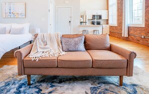 A modern living room with a brown sofa, a patterned throw blanket, and a blue and white rug. - Jennifer’s Penthouse Loft | State House City Views (Providence)