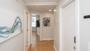 Un couloir doté d’un plancher en bois, de murs blancs et d’une porte située sur le côté droit.