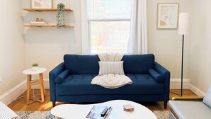 Un salon avec un canapé bleu, une petite table ronde, un lampadaire et des œuvres d’art accrochées aux murs.