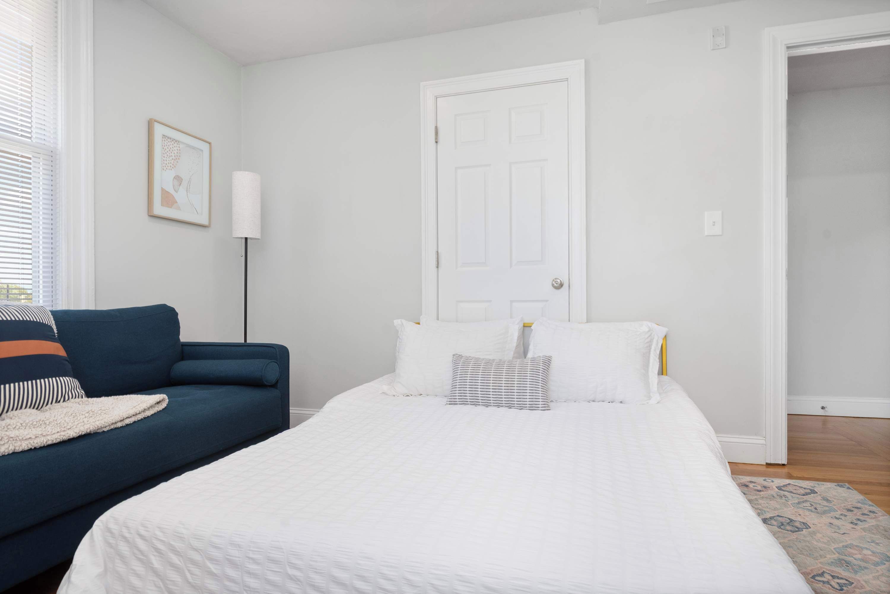 Une chambre à coucher avec un lit, un canapé bleu, une porte blanche et un tableau encadré au mur.