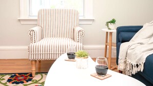Un fauteuil à rayures, un canapé bleu, une table basse blanche avec deux verres de vin rouge et une petite plante.