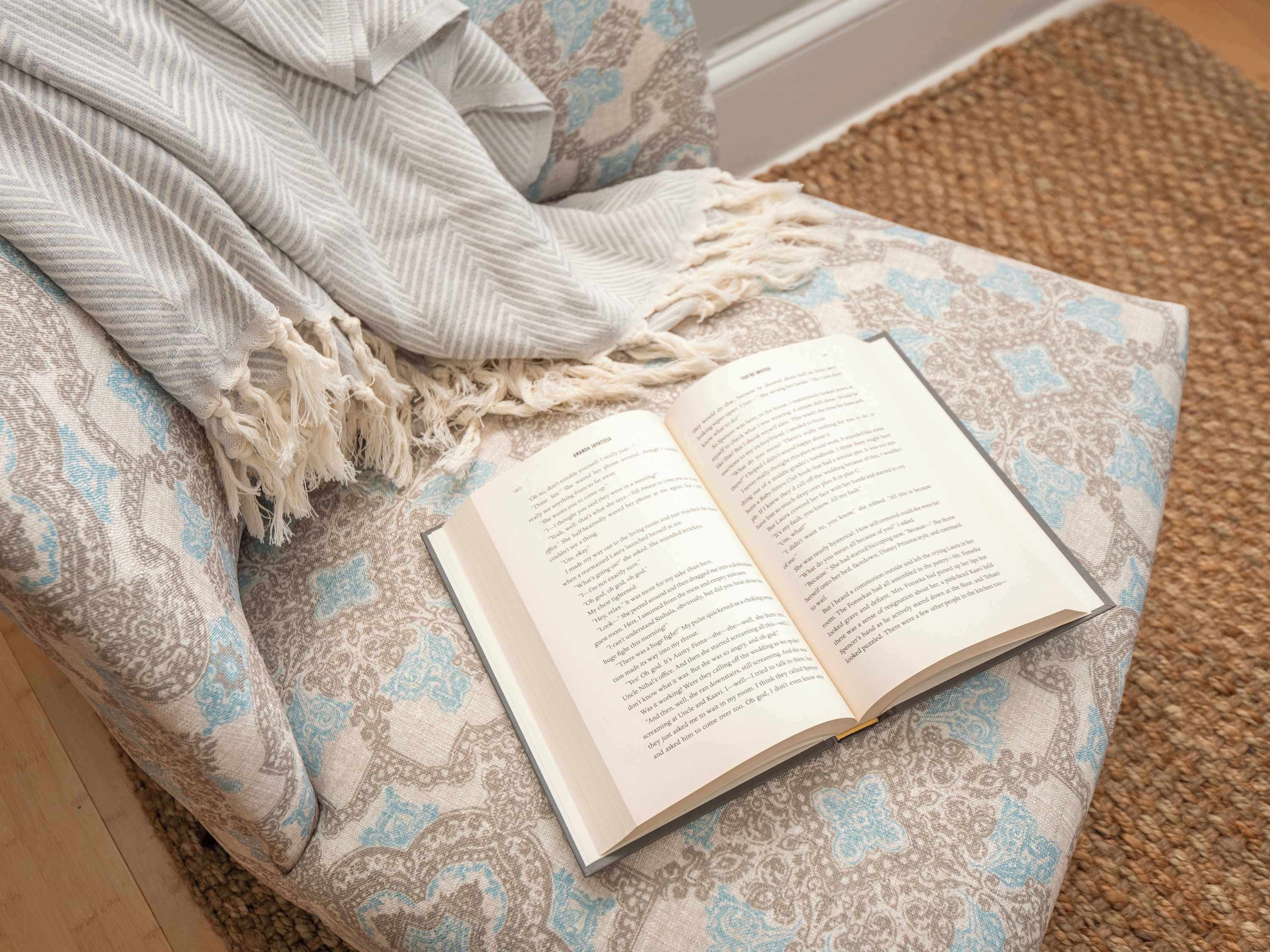 A book on a patterned ottoman with a throw blanket.
