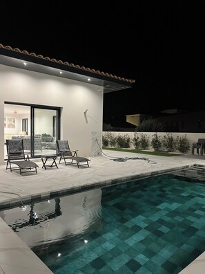 Un área de piscina moderna al aire libre con sillones de descanso y un patio bien iluminado.