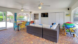 Uma sala ampla com móveis de vime, uma mesa de jantar com cadeiras coloridas e um ventilador de teto.