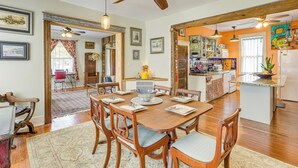 Een ruime eethoek met een houten tafel en stoelen, een plafondventilator, en een keuken met diverse apparaten en decoraties.
