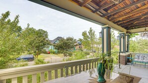 Een overdekt buitengebied met een houten terras, een glazen tafel en een groene vaas.