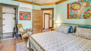 Een slaapkamer met een bed, een schommelstoel, een houten deur en een kleurrijk abstract schilderij aan de muur.