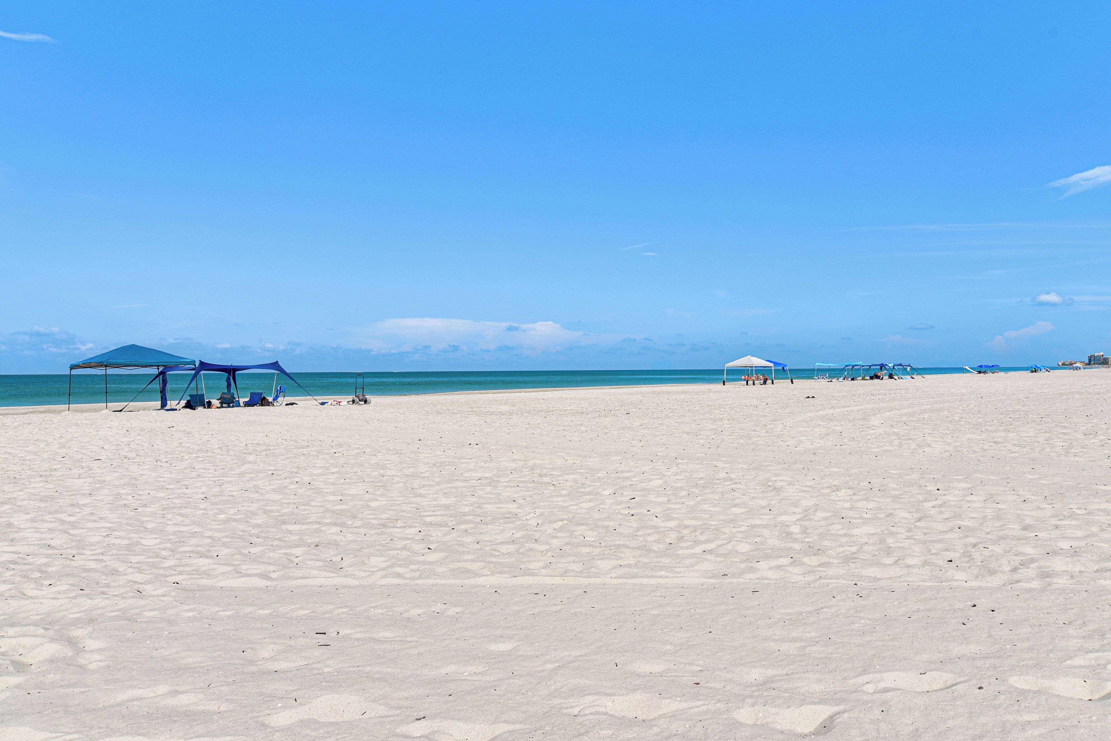 Ein Strand mit blauem Himmel, sandigem Ufer und einigen Sonnenschirmen.